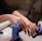 A close-up view of hands receiving a manicure, with a technician wearing blue gloves applying nail care. The nails are polished and well-groomed.